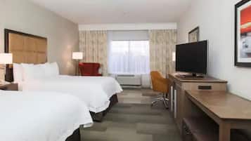 Una habitación de hotel con dos camas, un escritorio con televisor, una silla y una ventana con cortinas.