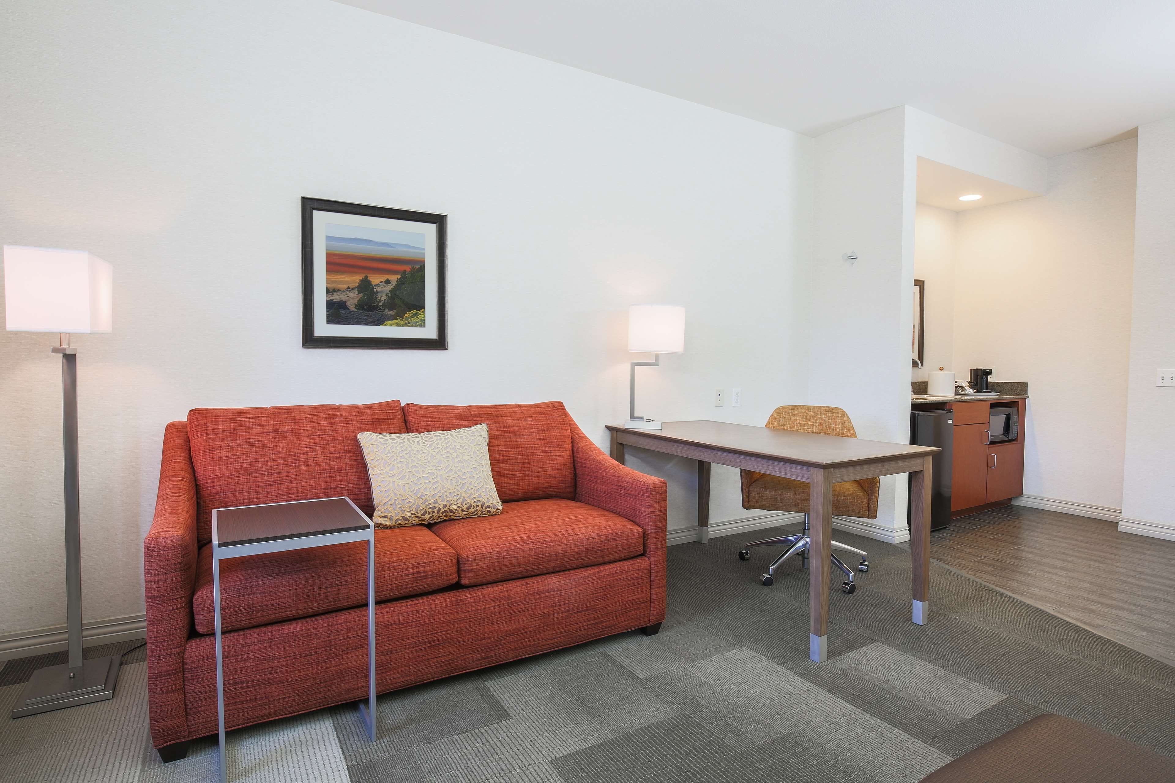 A compact room with a red sofa, a small table, a chair, and a kitchenette in the background.