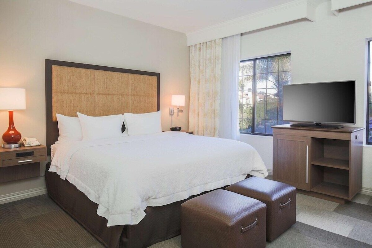 A hotel room with a large bed, a TV, a desk, and a window with curtains.