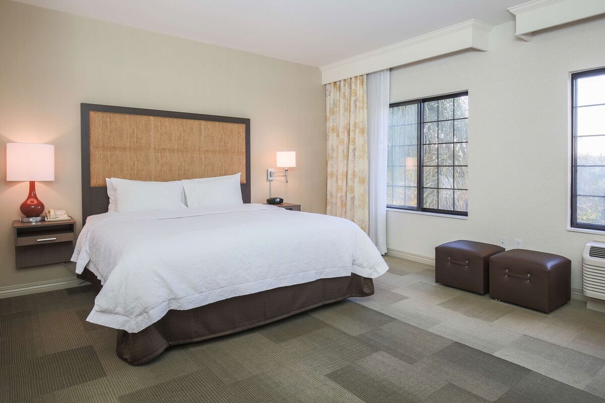 A hotel room with a large bed, bedside lamps, a window with a view, and a small seating area.