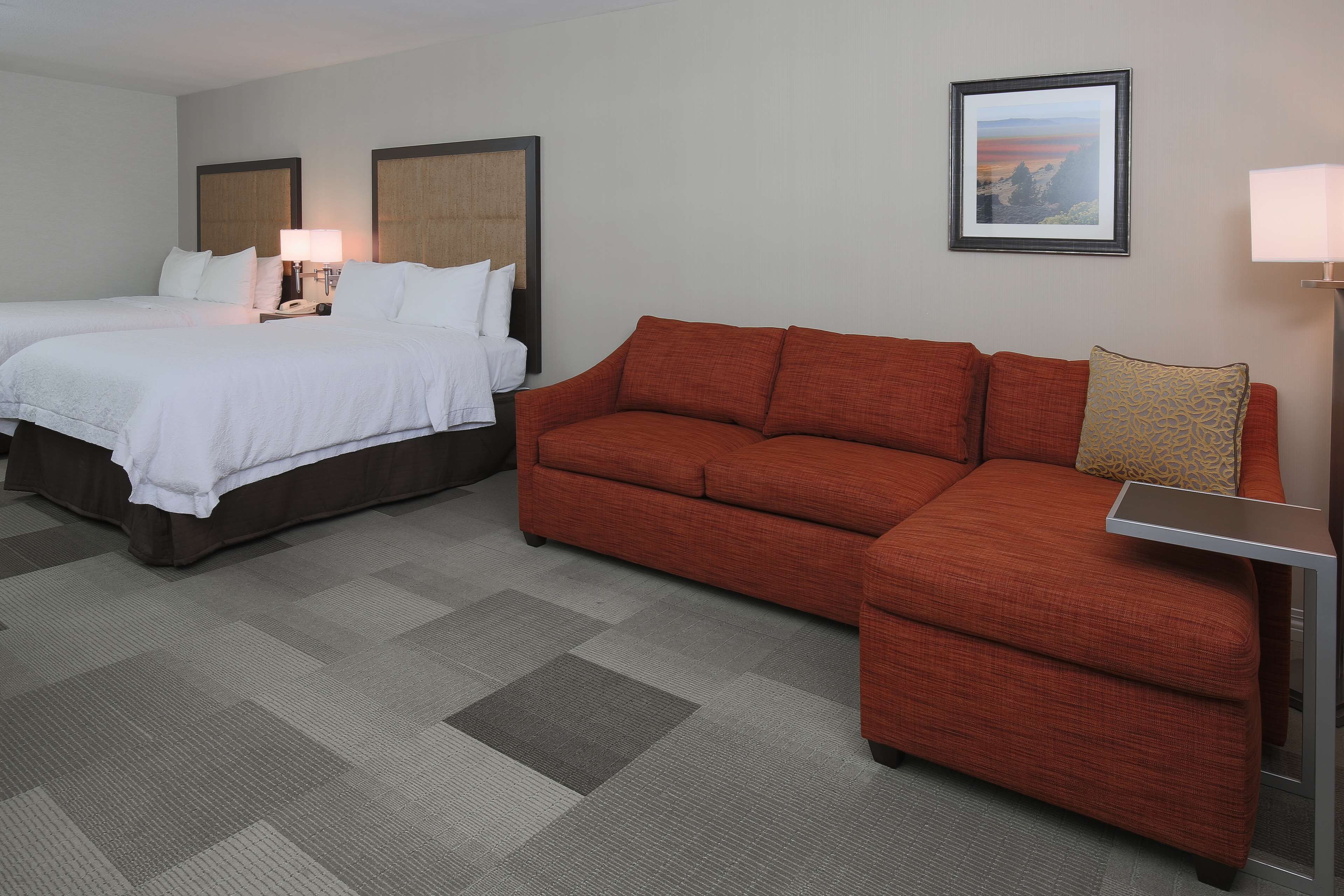 A hotel room with two beds, a red sofa, a small table, and a framed picture on the wall.