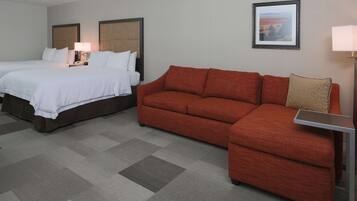 A hotel room with two beds, a red sofa, a small table, and a framed picture on the wall.