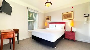 A hotel room with a bed, bedside tables, a desk, a chair, a TV mounted on the wall, and a window with a view of greenery.