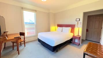 A hotel room with a bed, a desk, a chair, a lamp, and a bench.