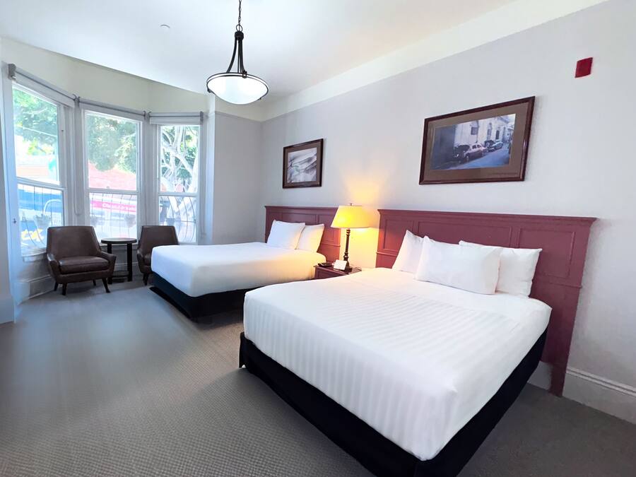 A hotel room with two beds, a sitting area with chairs, a table, and large windows.