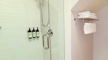 A modern bathroom with a glass-enclosed shower, a white tiled floor, and a towel rack with folded towels.