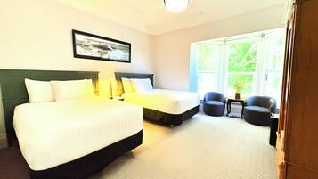 A hotel room with two beds, a chair, a desk, and a window with a view of greenery.