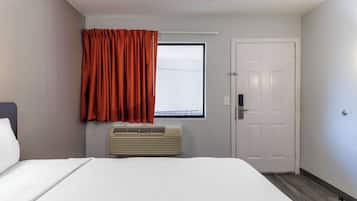 Habitación de hotel con cama, aire acondicionado, ventana con cortinas y una puerta.