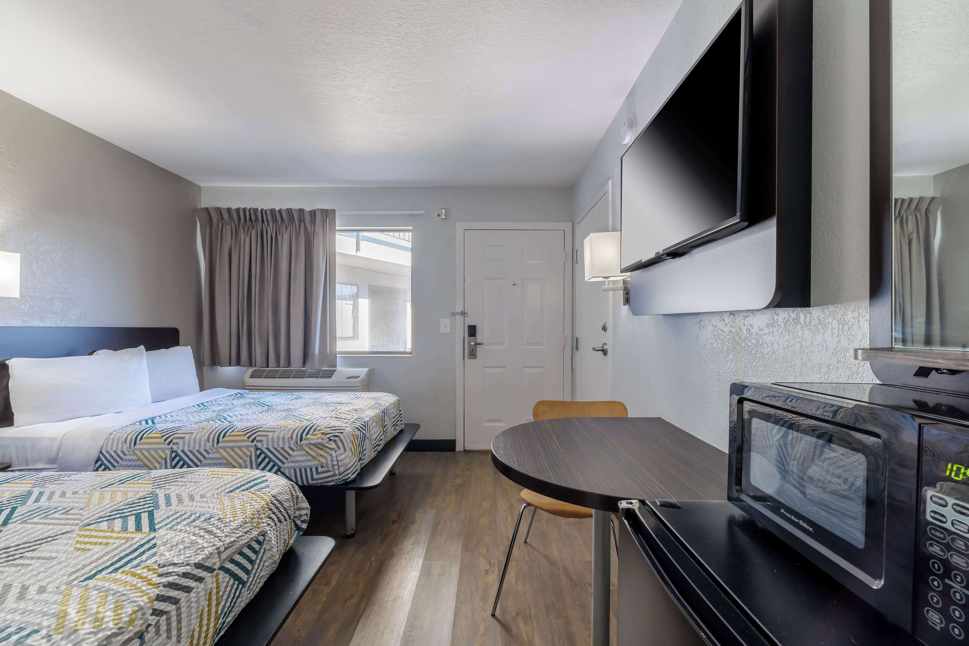 A hotel room with two beds, a dining table, a microwave, and a TV.