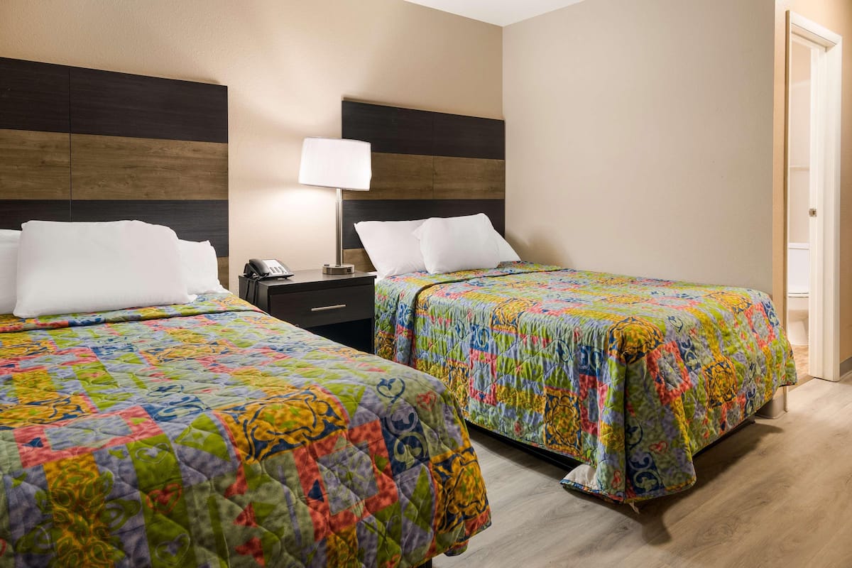 A hotel room with two beds, each with a colorful quilt, a bedside table with a lamp, and a wooden headboard.