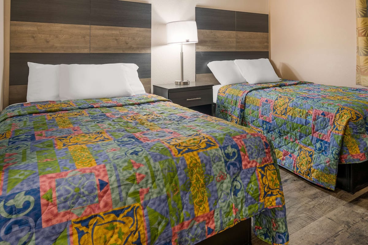 A hotel room with two beds, each with a colorful quilt, a nightstand with a lamp, and a wooden headboard.