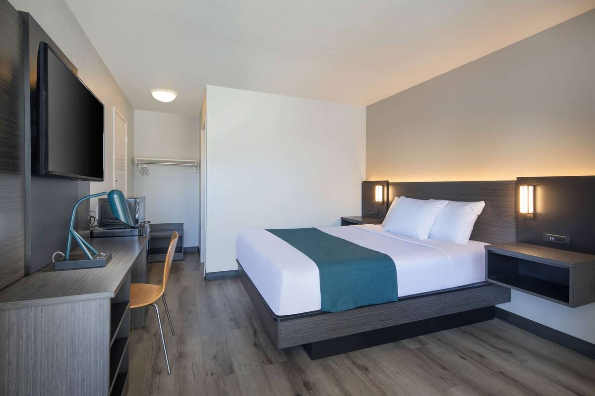 Ein modernes Hotelzimmer mit Bett, Schreibtisch, Stuhl und Fernseher.