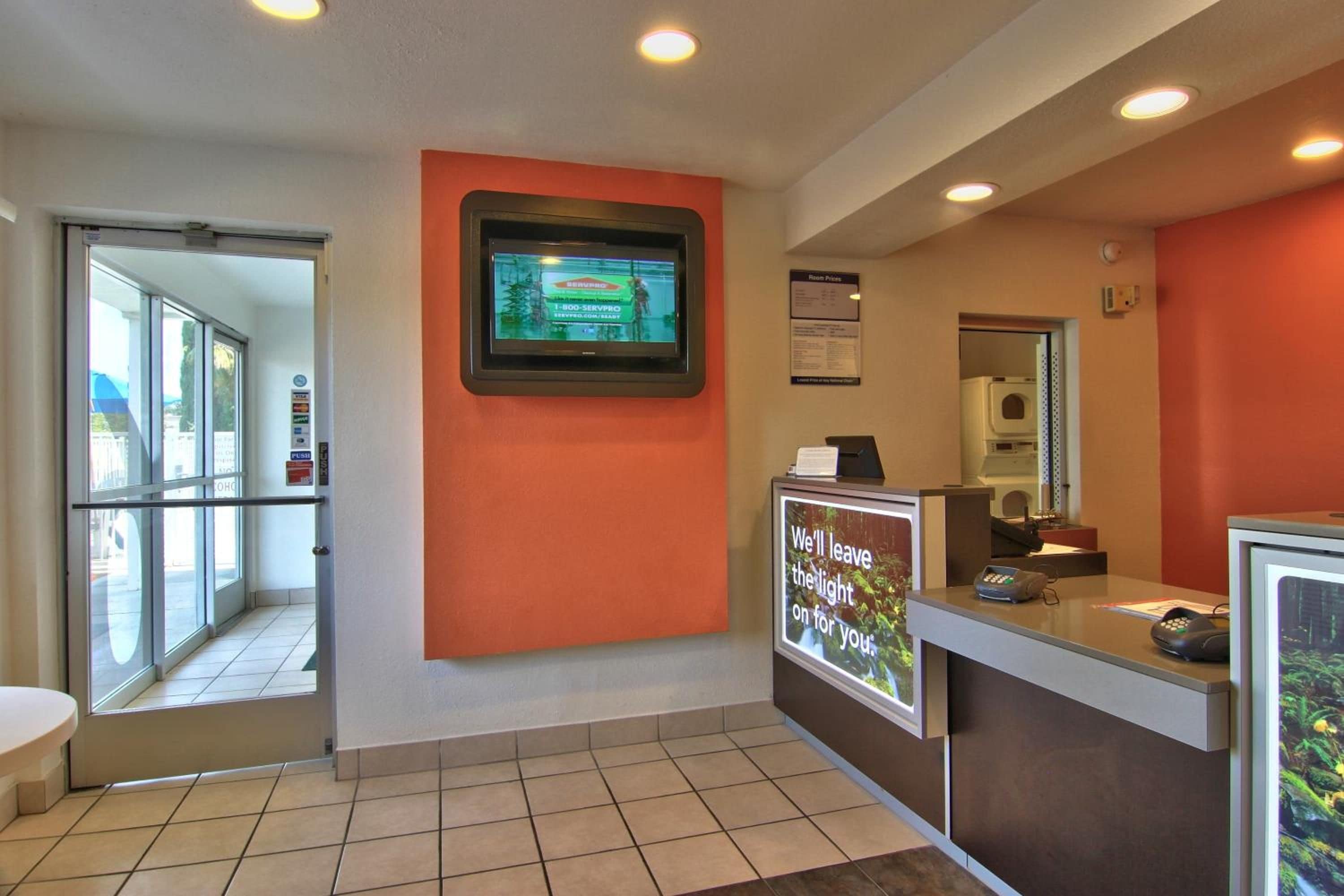 A hotel reception area with a digital screen, a counter, and a sign with a message.