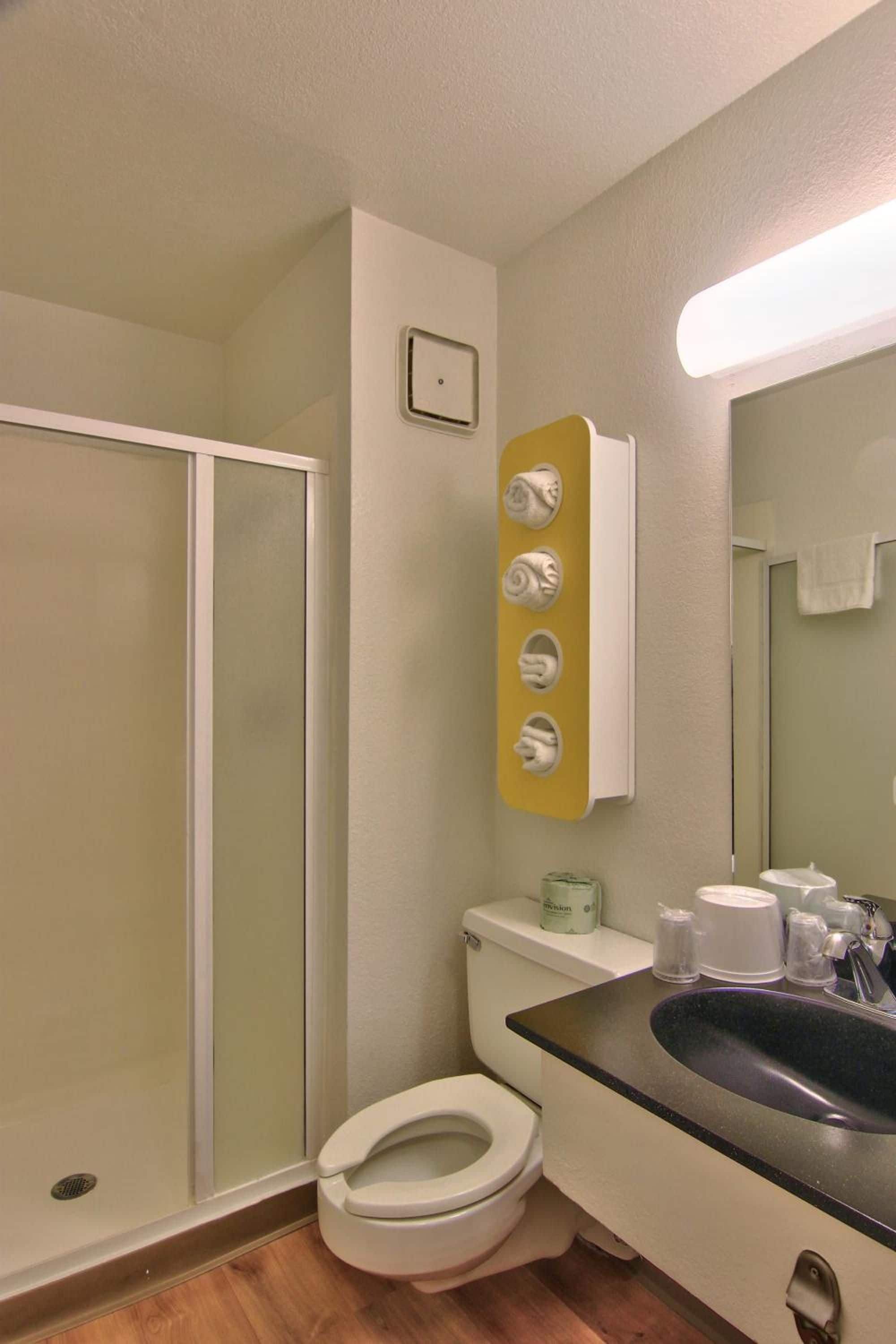A bathroom with a toilet, sink, and shower. There are towels and toiletries on the sink counter.