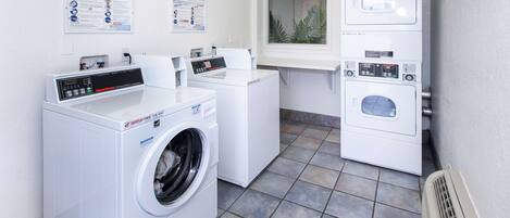 Une buanderie équipée d’un lave-linge à chargement frontal, d’un lave-linge à chargement par le haut et d’un sèche-linge. Des affiches d’information sont accrochées au mur, et un panneau indique que la buanderie n’est pas un endroit où l’on peut laisser des effets personnels sans surveillance.