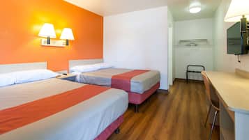 A hotel room with two beds, a desk, a chair, a TV, and a bathroom with a shower and a mirror.