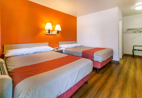 A hotel room with two beds, a wooden floor, and a wall-mounted lamp. - Motel 6 Rosemead, CA - Los Angeles (Rosemead)