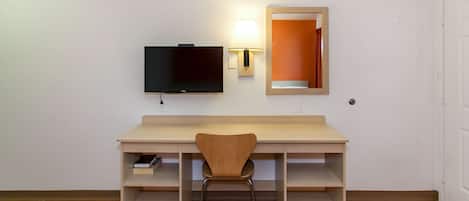 A room with a wooden desk, a chair, a television, and a wall-mounted lamp.