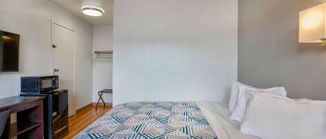 A hotel room with a bed, a desk with a microwave, and a small table.