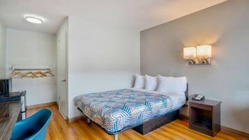 A hotel room with a bed, bedside table, lamp, and a desk with a chair.