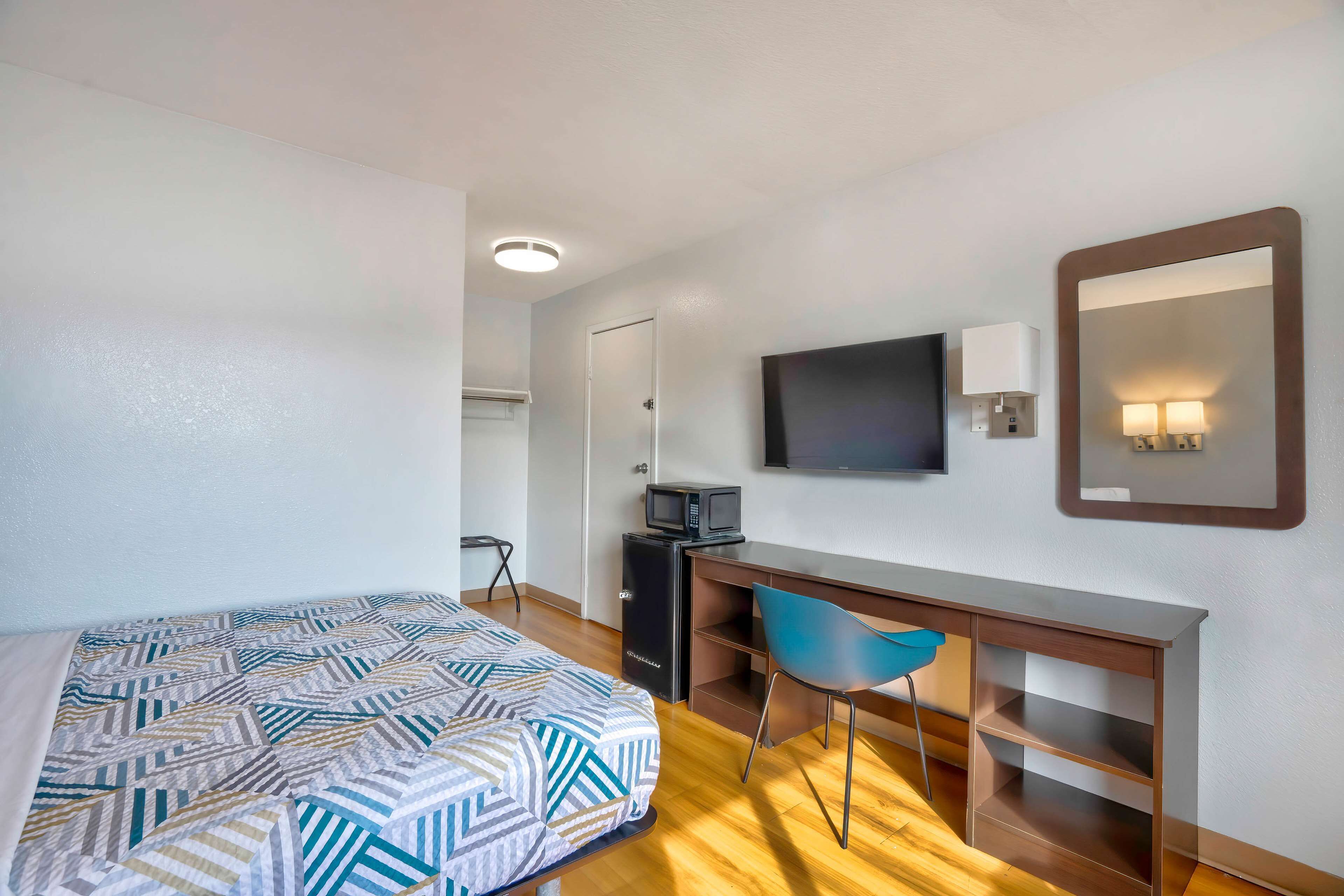 A hotel room with a bed, a desk, a chair, a television, and a mirror.