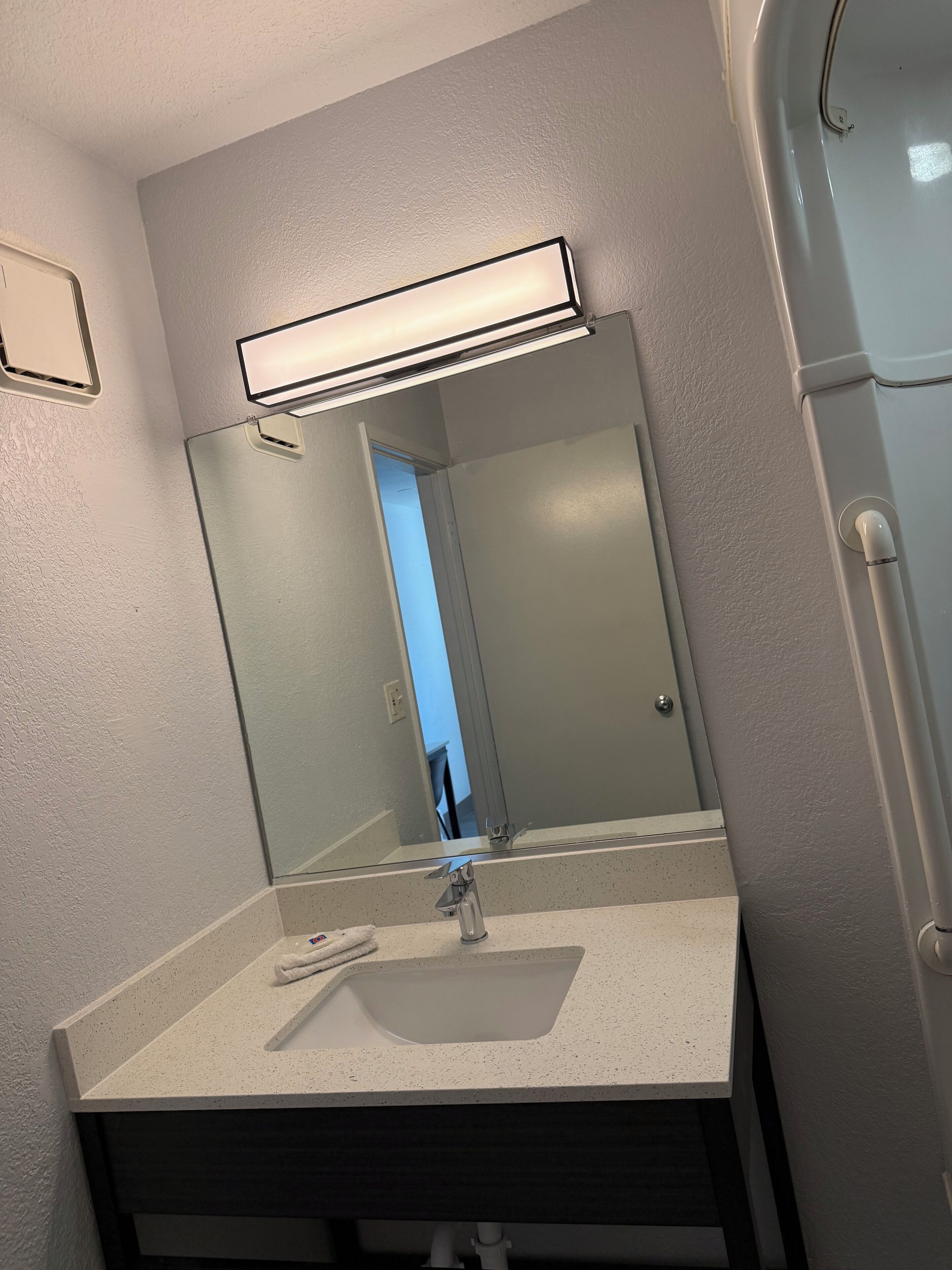 A bathroom with a mirror, sink, and a light fixture above the mirror.