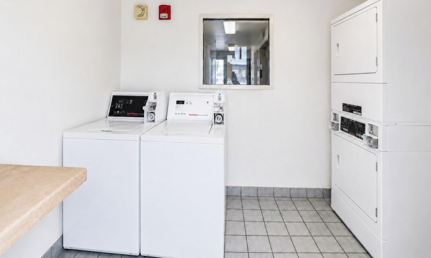 A laundry room with two front-loading washing machines and a dryer, a small window, and a tiled floor.