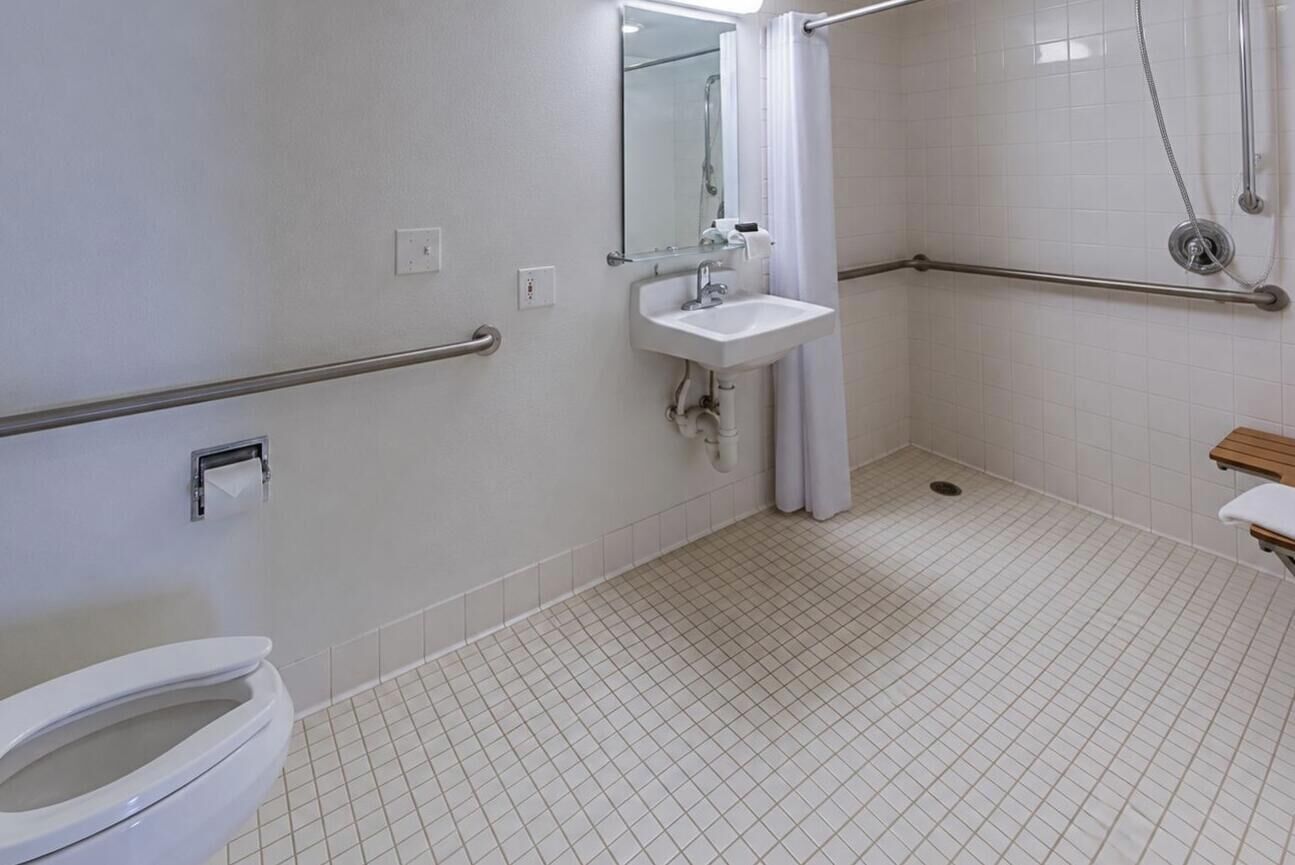 A bathroom with a toilet, sink, mirror, and shower area.