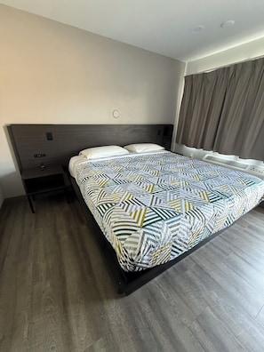 A hotel room with a bed, a nightstand, a wall-mounted phone, and a window with curtains. - Motel 6 Yreka, CA (Yreka)