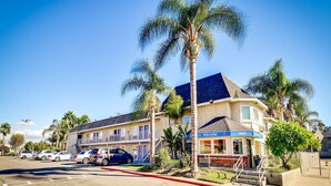 A two-story motel with a 'Welcome' sign, a parking lot with several cars, and palm trees. - Motel 6 Riverside, CA - South (Riverside)