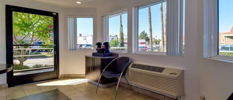 A hotel room with large windows, a chair, a desk, and a radiator.