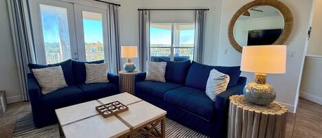 A living room with a sofa set, a coffee table, two lamps, a mirror, and a view of the outdoors.