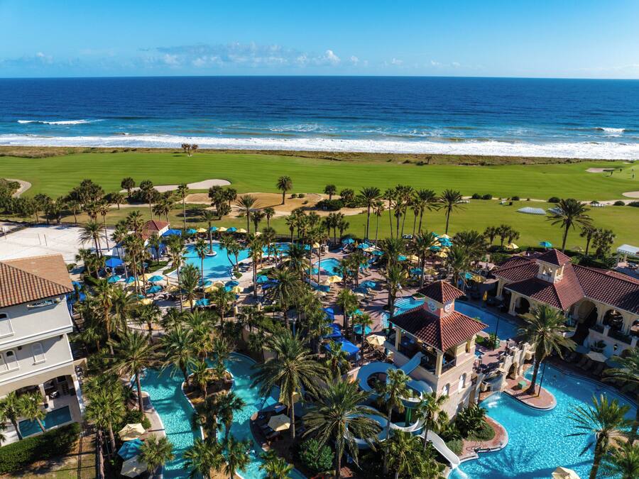 Um resort com várias piscinas, palmeiras e vista para o oceano.
