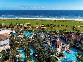 A resort with multiple swimming pools, palm trees, and a view of the ocean.