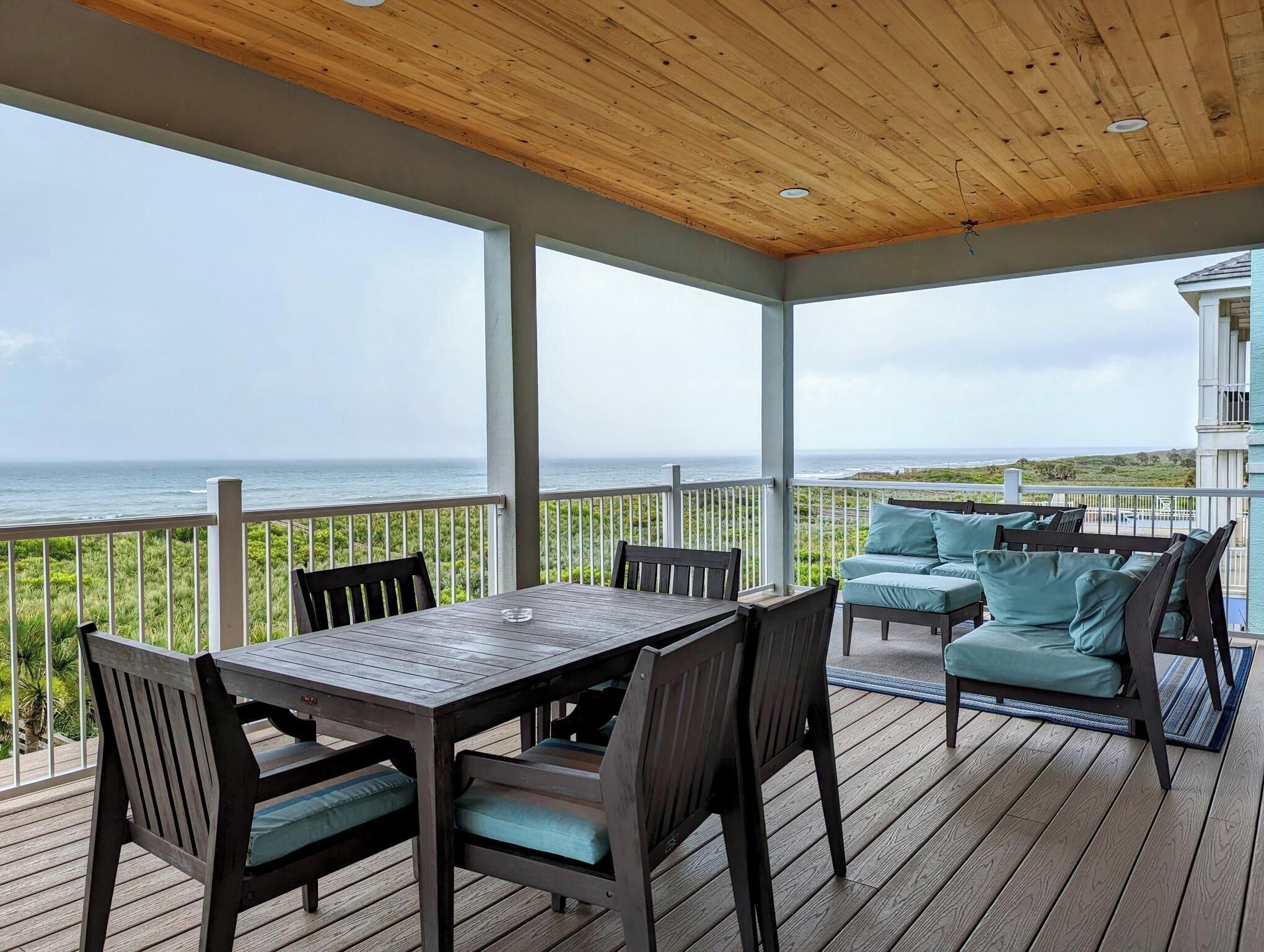 A covered outdoor deck with a table and chairs, overlooking the ocean.