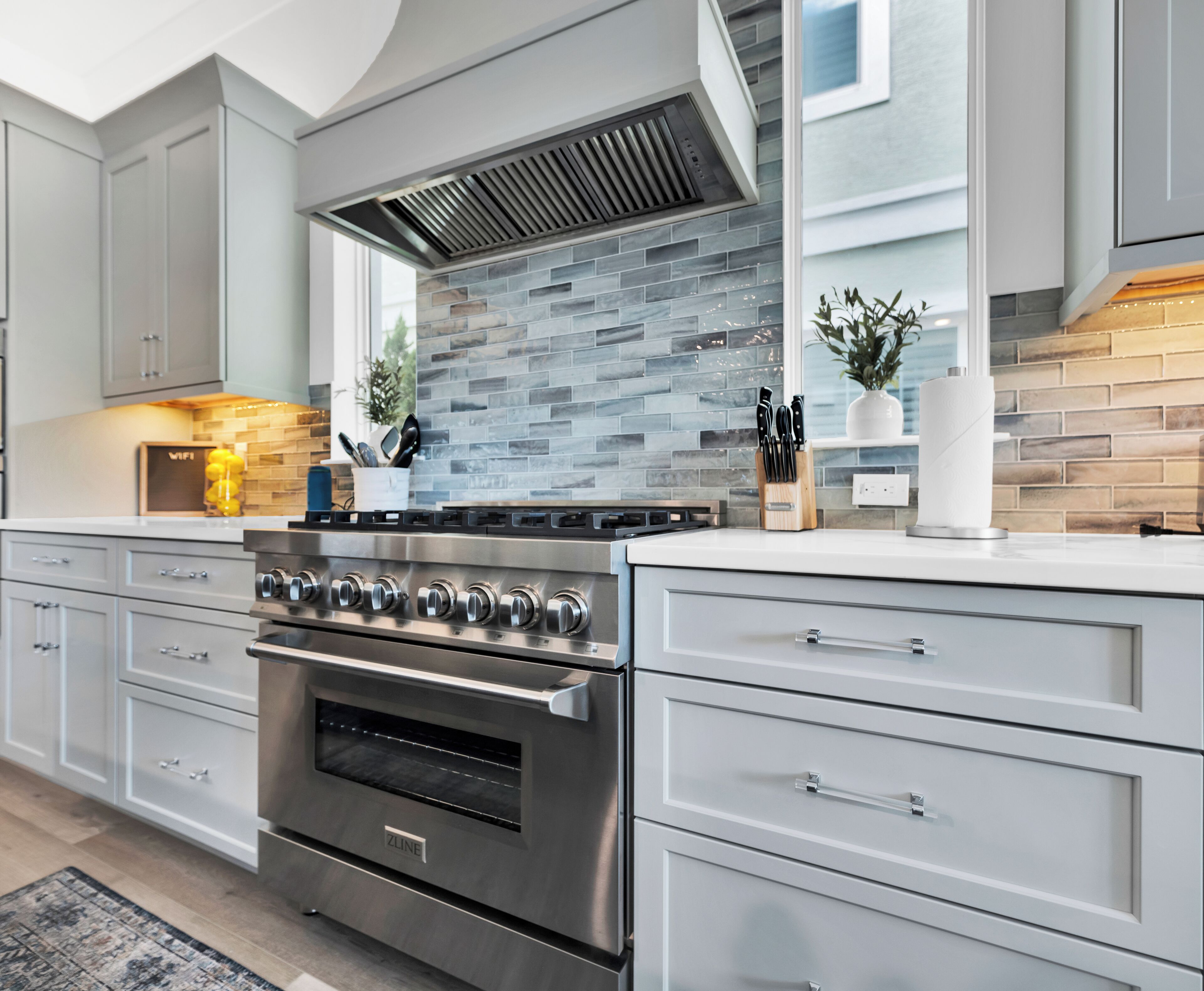 A modern kitchen with a stainless steel stove, grey cabinetry, and a tiled backsplash.