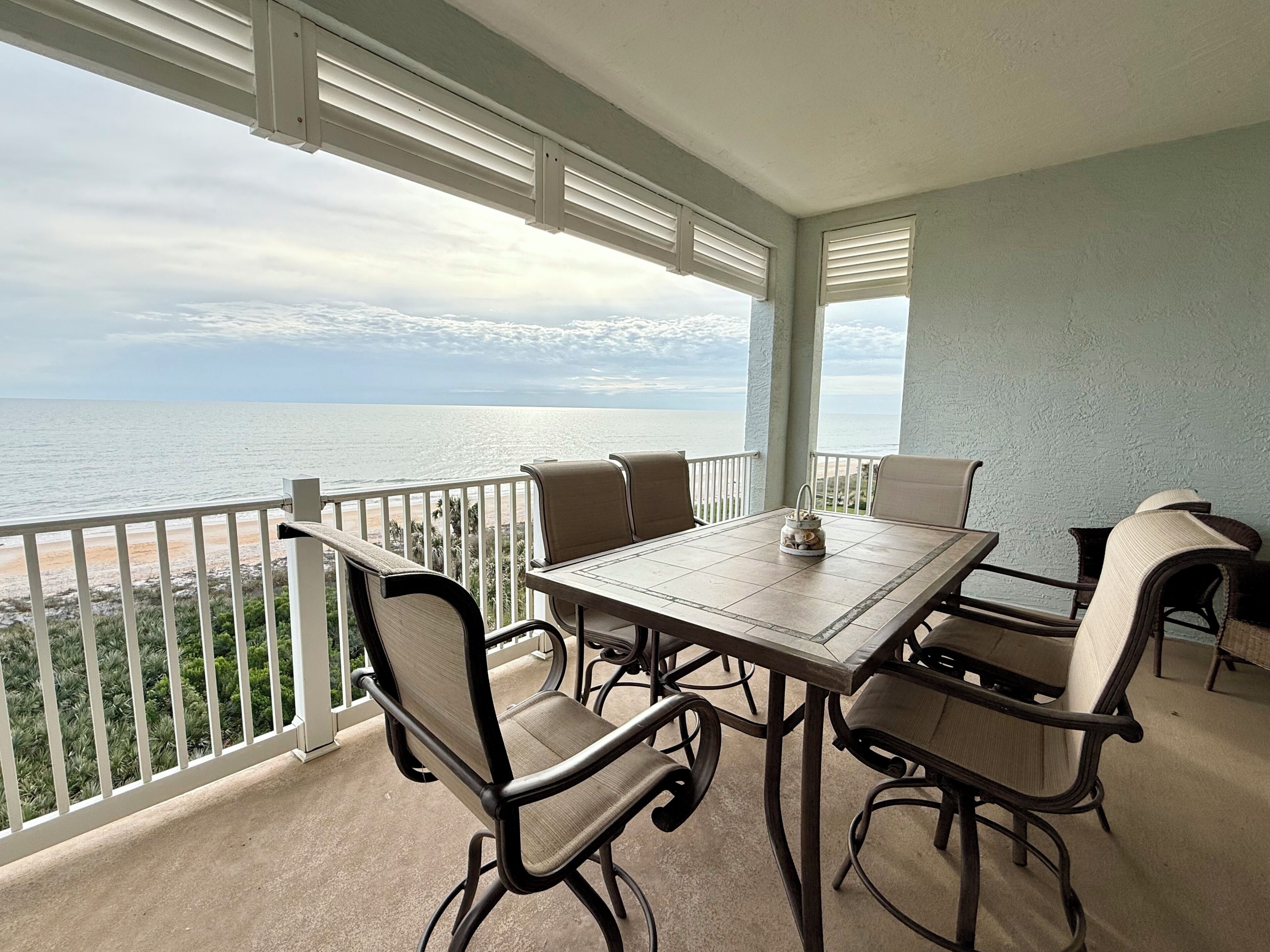 A balcony with a table and chairs, overlooking a beach and ocean.
