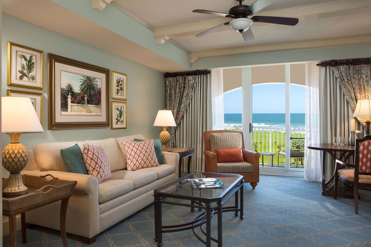 A living room with a sofa, armchairs, a coffee table, and a view of the ocean through large windows.