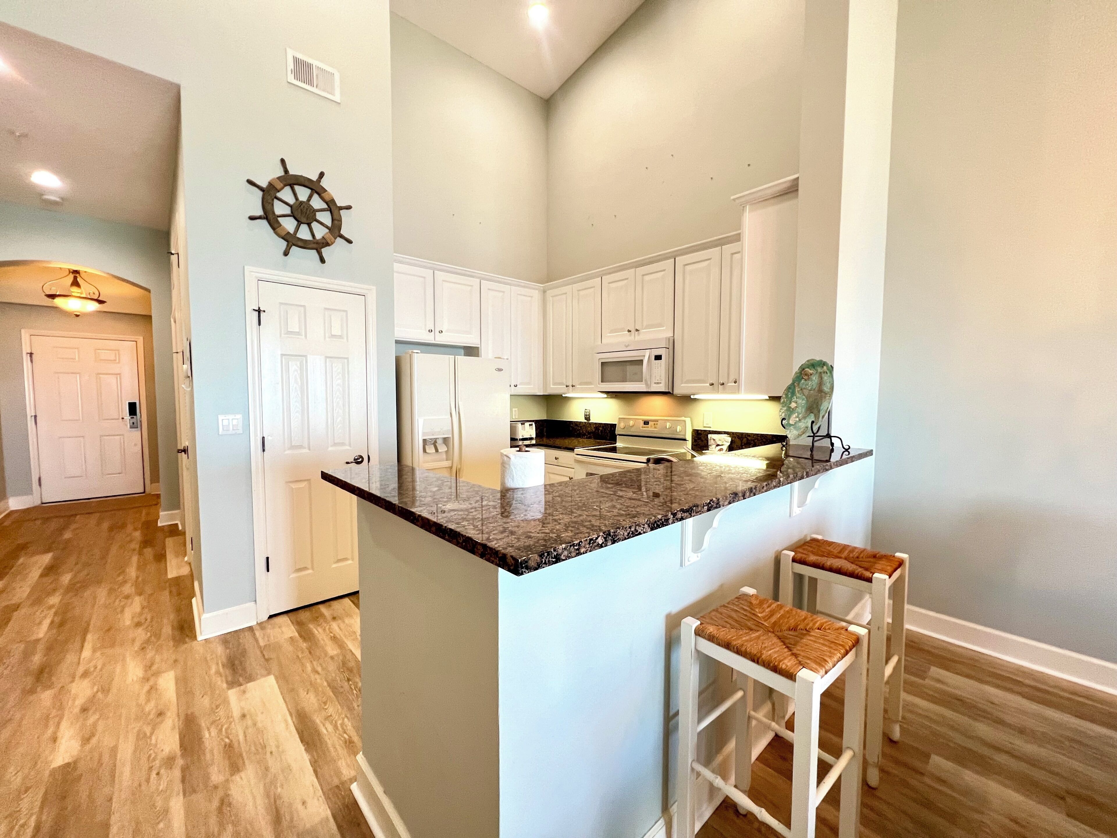 A kitchen with white cabinets, a granite countertop, and two bar stools.
