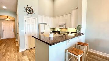 A kitchen with white cabinets, a granite countertop, and two bar stools.