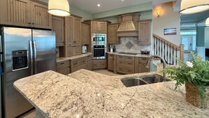 A kitchen with granite countertops, stainless steel appliances, wooden cabinets, and pendant lighting.