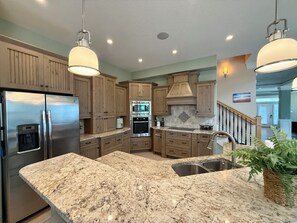 Una cocina con encimeras de granito, electrodomésticos de acero inoxidable, gabinetes de madera e iluminación colgante.