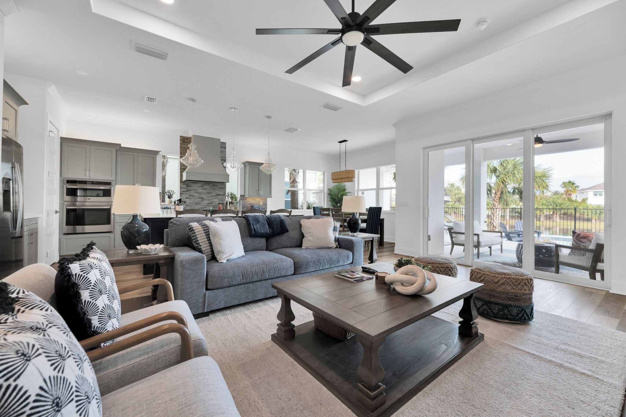 A spacious living area with a large sofa, coffee table, and dining table. There is a kitchen in the background with modern appliances.