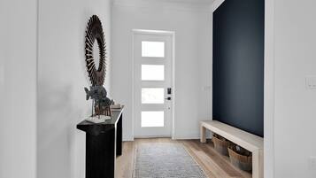Un pasillo con una consola negra, un adorno metálico, una puerta blanca, una pared de acento oscura, un banco de madera y una alfombra tejida.