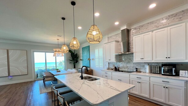 A modern kitchen with a large island, pendant lights, and a view to the outside.