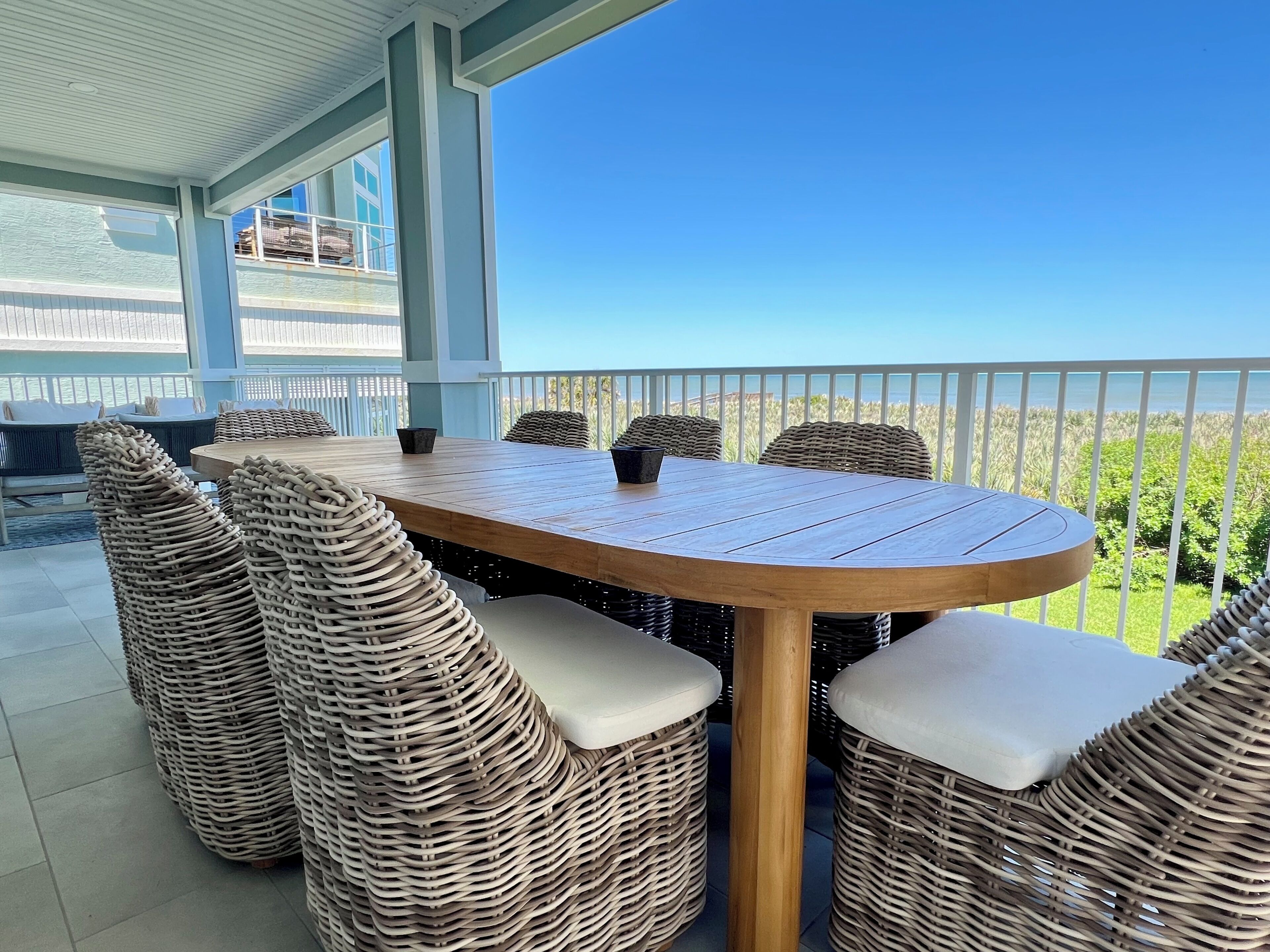 A covered outdoor dining area with wicker furniture and a view of the ocean.