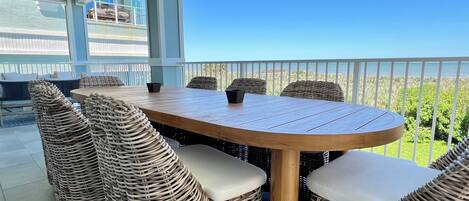 A covered outdoor dining area with wicker furniture and a view of the ocean.