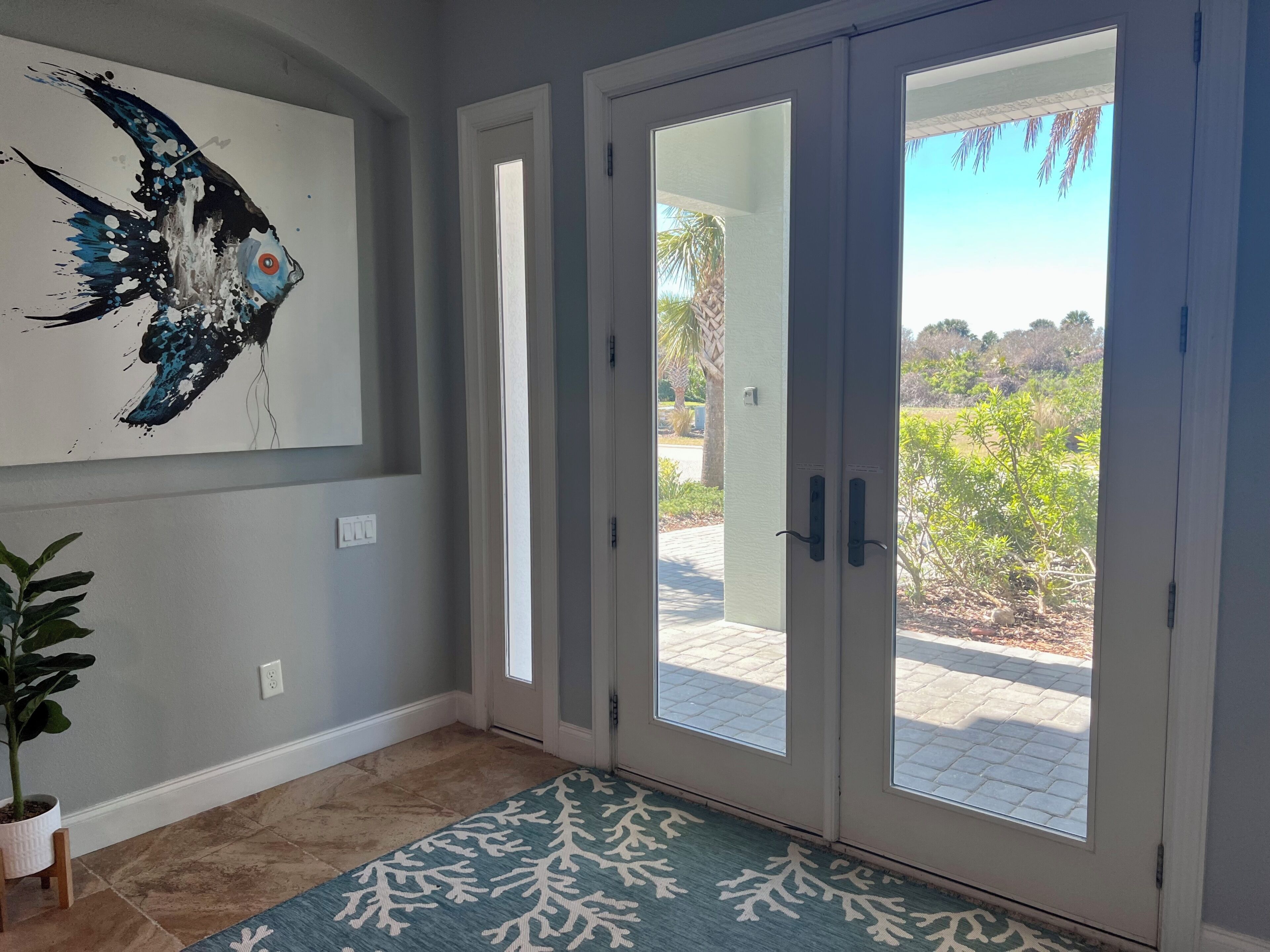 A room with a large fish painting, a potted plant, and a view through glass doors.