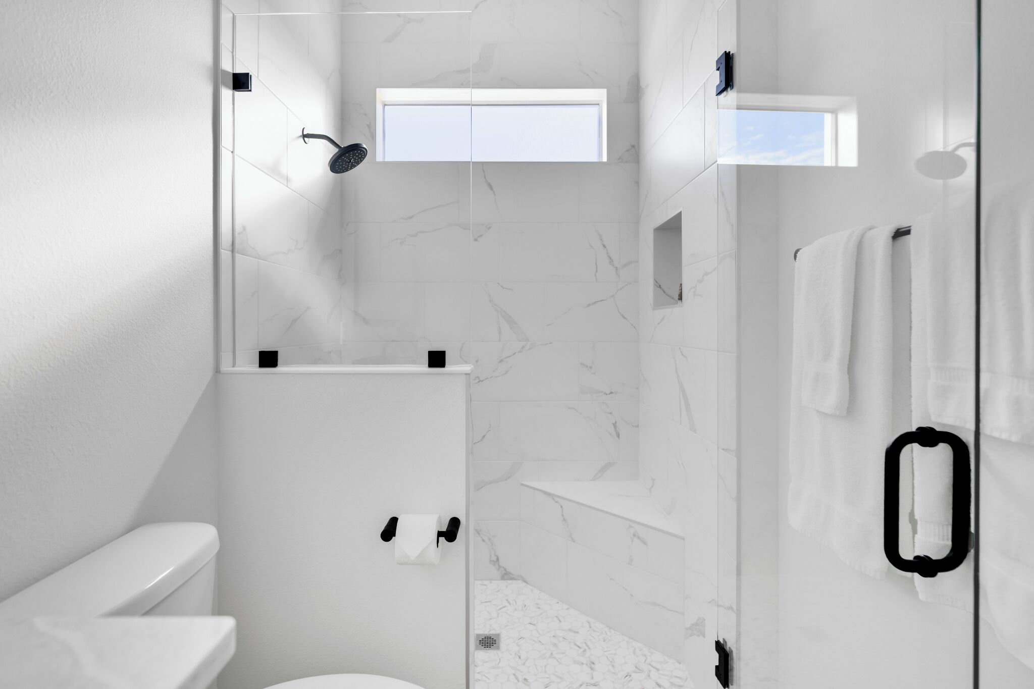 Un baño moderno con inodoro, ducha y zona de ducha con mampara de vidrio.