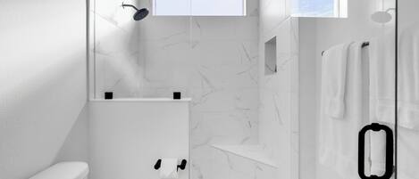 Un baño moderno con inodoro, ducha y zona de ducha con mampara de vidrio.